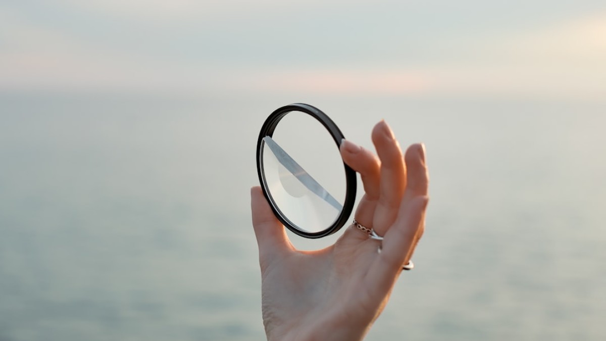 a hand holding a magnifying glass over a body of water